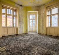 An abandoned room in a building with yellow walls and large windows.