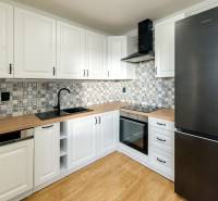 White kitchen in a 3-room apartment with wood-patterned flooring and patterned tiles.