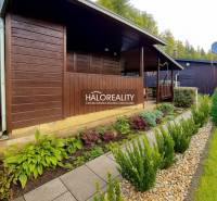 A wooden cottage in the gardens in Bytča, surrounded by well-maintained greenery and a path made of tiles.