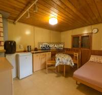 A room with a wooden decor floor, simple furnishings, a bed, and a kitchenette.