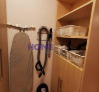 Storage space in a 2-room apartment with a vacuum cleaner and ironing board, wooden cabinets.