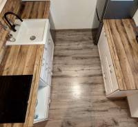 A kitchen in a 3-room apartment with a wooden decor floor and kitchen cabinets.