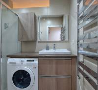 Bathroom with a shower in a 3-room apartment, washing machine and floor with wooden decor.