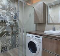 A bathroom with a washing machine, a shower, and a floor with a wooden decor in a 3-room apartment.