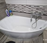 In the bathroom of the family house, there is a white bathtub with tiles and a faucet.