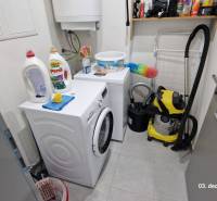 Laundry room in a family house with a washing machine, dryer, cleaning products, and a vacuum cleaner.