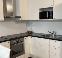 A kitchen in a studio apartment with white cabinets, a black countertop, and a wooden-patterned floor.