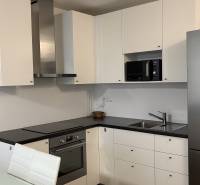 A kitchen in a studio apartment with built-in appliances, white cabinets, and a stainless steel refrigerator.