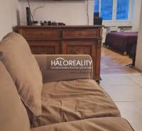 Living room with a sofa and a television, in the background a room with a wooden decor floor.