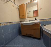 A bathroom in a 4-room apartment with a bathtub, blue tiles, and a cabinet with a sink.