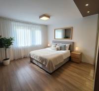 Bedroom with a bed, mirror, and nightstands in a 4-room apartment with a wood-patterned floor.