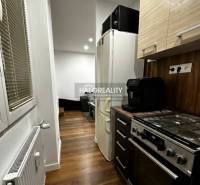 A kitchen in a studio apartment with a wood-patterned floor, a stove, and a refrigerator.