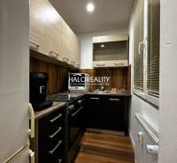 A kitchen in a one-room apartment with a wood-patterned floor and dark cabinets.