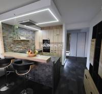 A kitchen in a 2-room apartment with a bar counter, stone cladding, and dark flooring.
