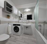 A bathroom in a 2-room apartment with a shower, a washing machine, and a floor with a wooden decor.