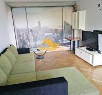 Living room with a sponge cake-colored couch, New York wallpaper, and a wood-patterned floor in a 3-room apartment.