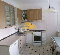 A kitchen with white cabinets, a gas stove, and a tiled floor in a three-room apartment.