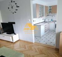 Living room in a three-room apartment with a wooden decor floor and a kitchen in the background.