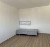 A simple room in a studio apartment with a bed and a wooden-patterned floor.