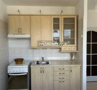 A kitchen in a studio apartment with a wooden decor and white tiles.