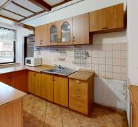 A kitchen in a family house with wooden cabinets, a tiled wall, and ceramic flooring.