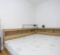 Bedroom in a studio apartment with a bed and wooden decor on the shelf.