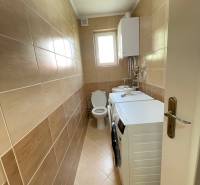 A narrow bathroom in a family house with a washing machine, toilet, and window.