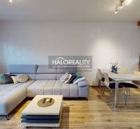 Living room with a corner sofa, table, and kitchen unit, floor with wooden decor.