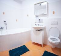Bathroom with a bathtub in a 3-room apartment; white tiles, orange floor tiles, blue rugs.