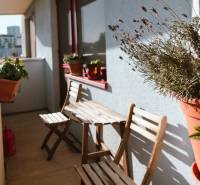 A balcony in a 3-room apartment with wooden seating and flowers on the edge.
