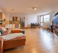 Living room in a three-room apartment with a wood-decor floor, corner kitchen, and dining table.