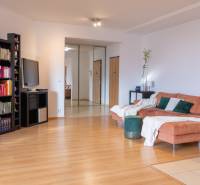 Living room of a 3-room apartment with a wooden decor floor, a shelf, and a comfortable orange sofa.