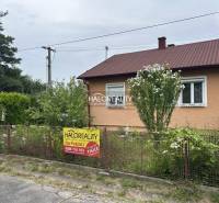The photograph shows a family house for sale, surrounded by a green garden and a fence.