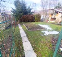 Garden plots in Malý Slivník with a walkway and vegetation, surrounded by a fence.