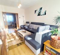 Living room with wood-patterned flooring and a gray sofa in a three-room apartment.