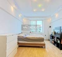 Bedroom in a 2-room apartment with a bed, dresser, wood-patterned floor, and wardrobe.