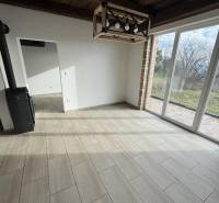 The interior of a cabin with a light wood-patterned floor, a fireplace, and large windows.