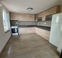 A kitchen in a cottage with light furniture, a wooden decor floor, and a large window.