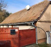 A family house in Brestovany with a red gate and roof, surrounded by greenery and a car.