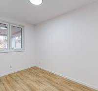 An empty room in a family house with white walls and a wooden-patterned floor.