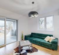 Living room with large windows, a green sofa, and a wood-patterned floor in a family house.