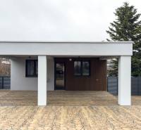 A family house in Nováčany with a paved terrace and a shelter. In the background, a church can be seen.