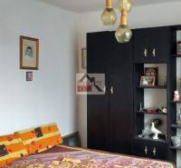 A bedroom in a family house with dark furniture, decorations, and enlarged photographs on the wall.