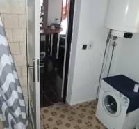 A bathroom in a cottage with a washing machine, shower curtain, and water heater.