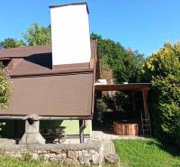 A cottage in Ružiná surrounded by greenery, outdoor seating, and a stone fireplace.