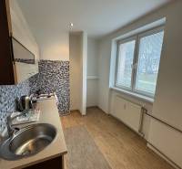 A kitchen in a 2-room apartment with a wooden decor floor and mosaic tiles.