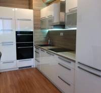 A kitchen in a 2-room apartment with glossy white cabinets and a floor with a wood decor.