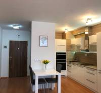 A kitchen with white furniture and a dining table in a 2-room apartment, flooring with a wooden decor.