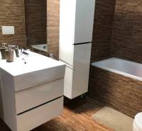 A bathroom in a 2-room apartment with brown tiles, white furniture, and a bathtub.