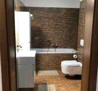 A bathroom with brown tiles, a sink, and a toilet in a 2-room apartment.
